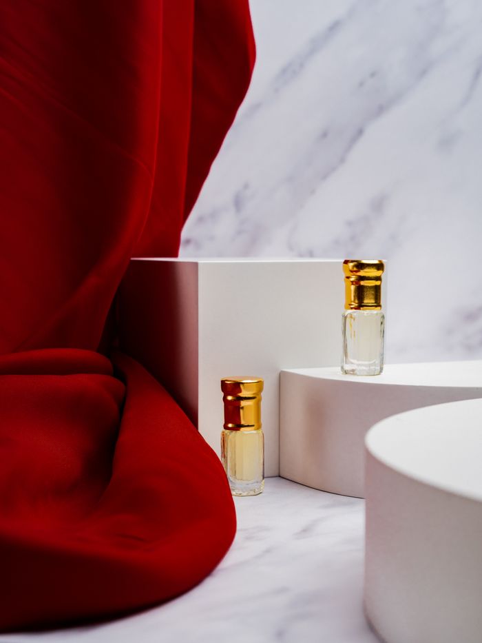 Offerings Stylish product photography of perfume bottles with golden caps set against a marble and red fabric backdrop.