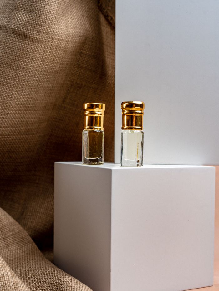 Offerings Close-up of two elegant perfume bottles with gold caps on a minimalist white display, evoking luxury.